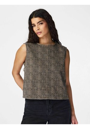 Kobieta o długich, ciemnych włosach, ubrana w bezrękawnik w panterkę i czarne spodnie, pozuje z jedną ręką za plecami na białym tle.