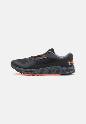 Baskets de sport noires avec un dessus texturé, des accents gris, des détails orange, une semelle à motif camouflage et un système de laçage pour un maintien sécurisé.