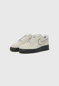 Gray suede sneakers with a black rubber sole, featuring textured perforations, a curved swoosh logo, and classic lace-up design.