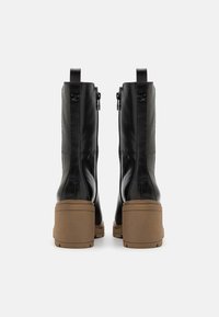 Bottines en cuir noir avec un talon épais couleur tan, dotées de zips latéraux et de languettes pour un enfilage facile, texture lisse et design épuré.