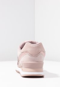 Vaaleanpunaiset lenkkarit, joissa on sileä mokkanahkapinta, läpirei'itetyt yksityiskohdat, pehmustettu nilkkaosa ja valkoinen välipohja, jossa on teksturoitu kantapää.