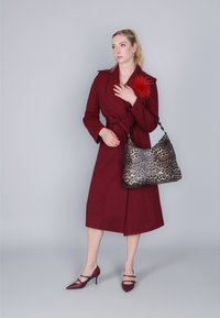 Bordeauxfärgad omslagsoverall med knytmidja, i kombination med en väska med leopardmönster och bordeauxfärgade högklackade skor. Röd fjädraccent på kappan.