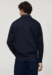 Námornícky sveter vyrobený z jemnej látky, s golierom a rebrovanými manžetami, vo voľnom strihu a s jednoduchým, čistým dizajnom. Zobrazený pohľad zozadu.