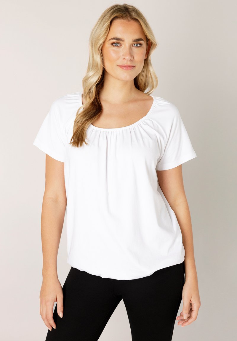 White short-sleeve top with a scoop neckline and gathered detail at the front, made of soft fabric, paired with black pants.