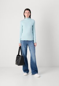 Lichtblauwe lange mouwen top met een franje hals, gepaard met wijde blauwe jeans en een zwarte totebag. Witte sneakers maken de look af.