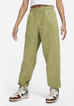 Osoba w jasnozielonych dresach Nike Air z teksturowanymi panelami i wielokolorowymi wysokimi trampkami, stojąca na białym tle.