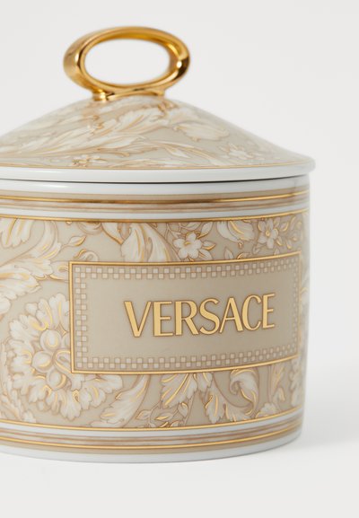 Keramikas burka ar zelta rokturi, bēšā krāsā ar ziedu rakstu, zelta akcentiem un centrālo "VERSACE" etiķeti taisnstūra rāmītī.