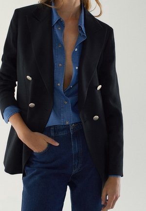Black double-breasted blazer with metallic buttons, layered over a blue denim shirt. Features a notched collar and fitted silhouette.