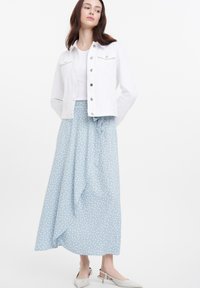 Bijela traper jakna preko bijele bluze, uparen s svijetloplavom suknjom s točkicama u obliku ovogood koji se veže, i bež slingback cipelama.