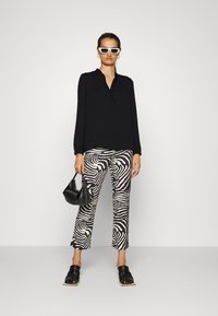 Zwarte blouse met lange mouwen; zwarte en witte zebra-gepatroneerde broek; zwarte handtas; zwarte blokhak sandaaltjes; witte zonnebril.