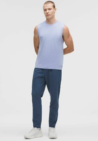 Šviesiai mėlynas be rankovių marškinėliai su tekstūriniais akcentais, derinami su tamsiai mėlynomis siaurėjančiomis kelnėmis ir baltomis sportinėmis bateliais. Paprastas, šiuolaikinis dizainas.