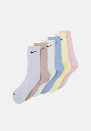 Septiņi riboti kokvilnas maisījuma zeķu komplekti pasteļa krāsās: lilā, bēšā, baltā, zilā, dzeltenā un rozā, ar melniem Nike logo akcentiem.