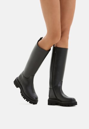 Schwarze kniehohe Stiefel aus glattem Material mit dicker Sohle und seitlichem Reißverschluss, die ein sauberes Design und minimale Details aufweisen.