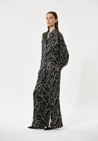 Sorte og hvide geometriske mønstrede sæt bestående af en langærmet skjorte og brede bukser, med en glat, ensartet tekstur og lommer.