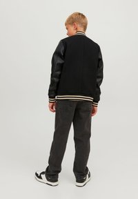 Svart varsityjacka med läderärmar, randig ribbad krage och mudd. Bärs med mörkgrå jeans och svarta sneakers.