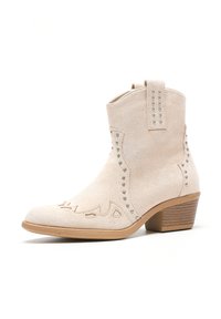 Stivaletto in suede beige con tagli decorativi e borchie in argento. Presenta un tacco basso a blocco e un serraggio per facilitare l'indossatura.
