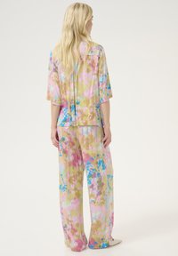 Completo a due pezzi composto da una camicia a maniche corte e pantaloni a gamba larga, realizzato in tessuto leggero con un vivace motivo floreale nei colori rosa, blu e giallo.