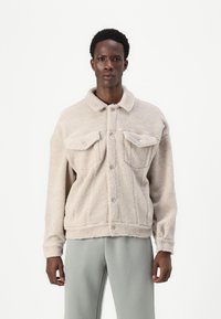 Beige fleecjacket met een knoopsluiting aan de voorkant, twee borstzakken en een gespreide kraag. Kenmerkt zich door een gestructureerde, zachte stof en een losse pasvorm.