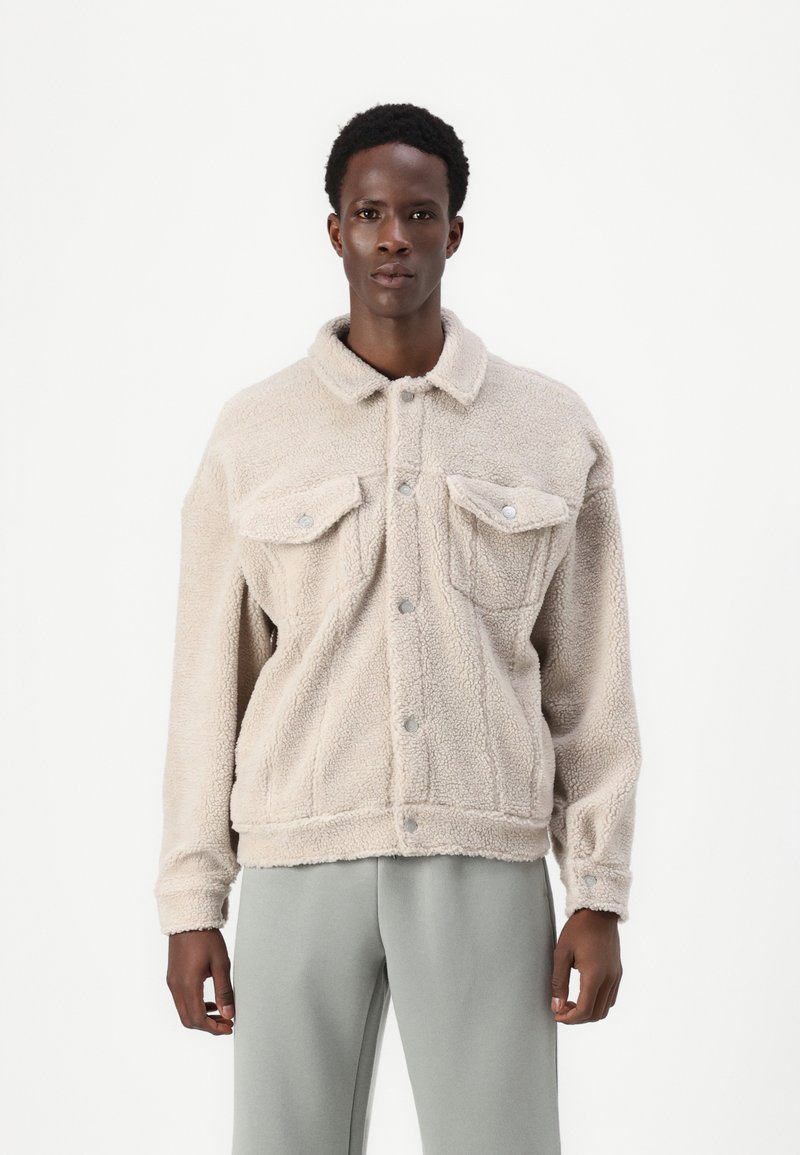 Beige fleecjacket met een knoopsluiting aan de voorkant, twee borstzakken en een gespreide kraag. Kenmerkt zich door een gestructureerde, zachte stof en een losse pasvorm.