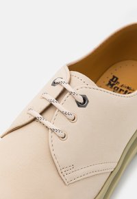 Béžová kožená bota s hladkým povrchem, zaoblenou špičkou, černými dírkami na tkaničky a světlými tkaničkami. Interiér obsahuje polstrovanou stélku s perforacemi.