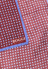 Siidine taskuruut, millel on punane ja sinine geomeetriline muster väikestest ruutudest, valge tikandiga BOGGI MILANO sildiga.