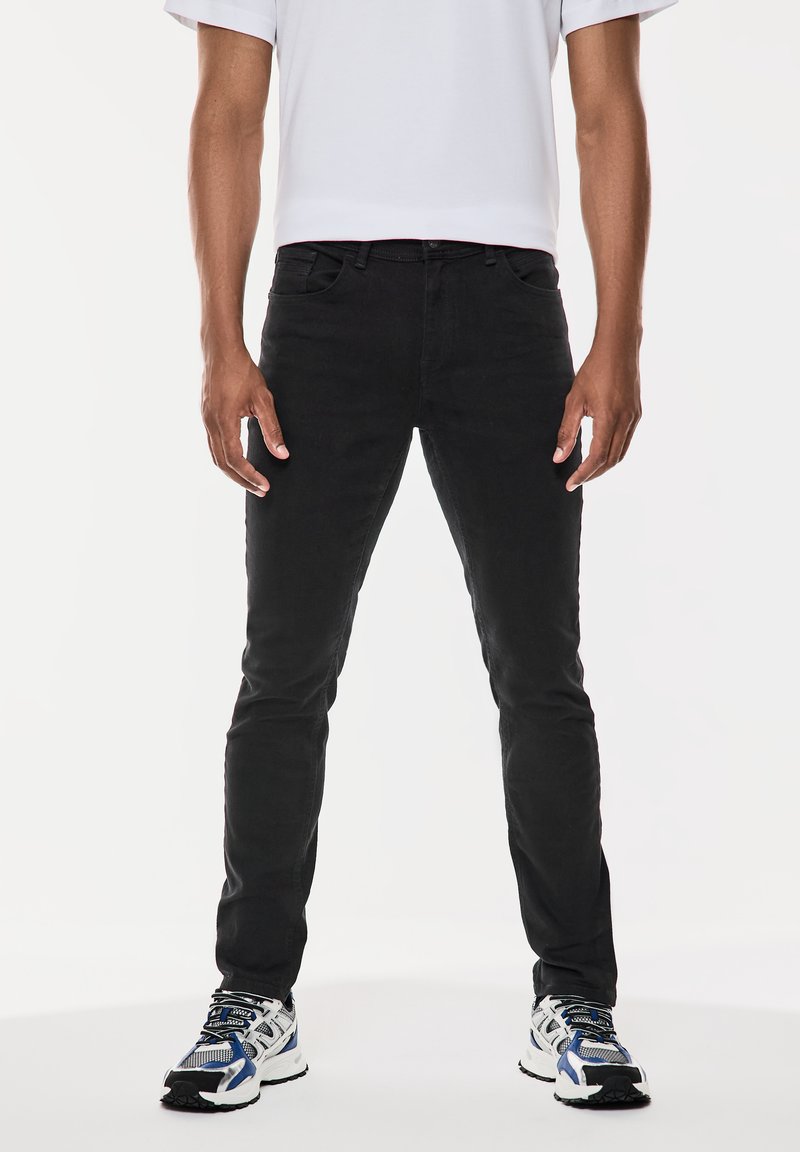 Svarta slim-fit jeans i bomull med en slät textur, matchade med blå och vita sneakers med nätöverdrag och svart sula.