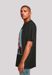 Black t-shirt with short sleeves, featuring a bold graphic design on the front in red, blue, and yellow. Relaxed fit, cotton material.