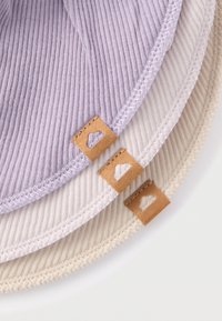 Trzy okrągłe elementy z tkaniny w kolorach jasnofioletowym, beżowym i kremowym. Każdy ma teksturowany, żebrowany wzór oraz brązową skórzaną metkę z wyciętymi detalami.