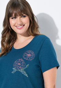 Sininen puuvillapaita, jossa on kukkakirjontaa vaaleanpunaisena ja vihreänä. Lyhyet hihat ja pyöreä kaula-aukko. Pehmeä pinta ja rento mitoitus.