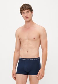 Navy blue cotton trunks with a fitted design, featuring a textured waistband with white brand lettering. The fabric appears smooth and stretchy.