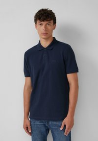 Tumedat sinine polo särk, mis on valmistatud puuvillast, klassikalise krae, kolme nööbiga kinnituse ja lühikeste varrukatega. Kandmine denimsiniste teksadega.