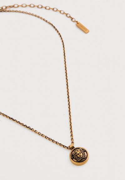 Χρυσή αλυσίδα με στρογγυλό μενταγιόν που απεικονίζει σχεδιασμό με λεπτομερή κεφαλή της Μέδουσας σε λευκό φόντο.