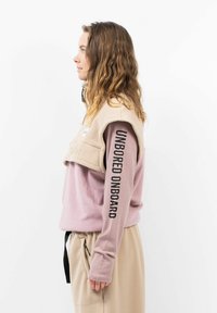 Fleece-Pullover mit beigem Oberteil und pinkem Unterteil. Mit schwarzem Text auf dem Ärmel und einem hohen Kragen. Weiche Textur mit lockerer Passform.