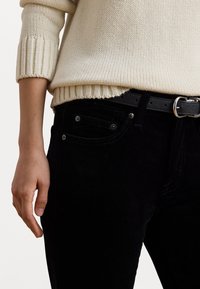 I pantaloni in corduroy neri presentano una vestibilità slim, tasche frontali a toppa con dettagli in metallo, abbinati a un maglione a maglia crema aderente e una cintura nera.