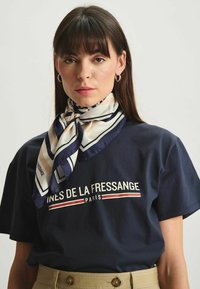 T-shirt marine avec graphique "Ines de la Fressange Paris", associé à un foulard en soie à motifs crème, marine et rayures.