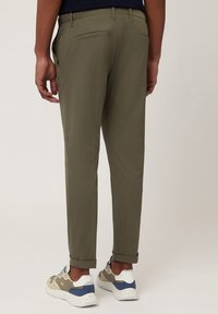 Chinos vert olive avec une coupe slim, texture lisse, deux poches arrière et ourlets retroussés au-dessus des chevilles, associés à des baskets blanches décontractées.
