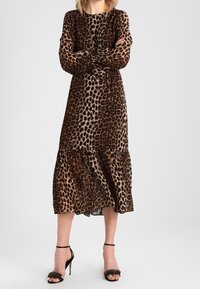 Midiklänning i leopardmönster med långa ärmar, insvängd midja, tärnad fåll och lätt material. Matchad med svarta klacksandaler.