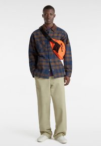 Rutigt skjorta i blått och brunt, beige krage, matchad med ljusbeige byxor och en ljusorange axelväska. Vita skor fulländar outfiten.