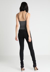 Jeans skinny negros combinados con una camiseta sin mangas ajustada de color gris metálico con tirantes finos. La camiseta tiene un acabado texturizado que presenta un sutil brillo.