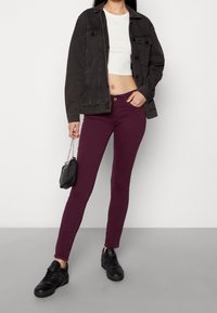 Svart denimjacka med två framfickor, vit kortärmad skjorta, vinröda skinny jeans och svarta sneakers. Liten svart handväska med kedjesnodd.