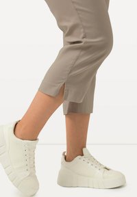 Pantaloni beige a vita alta con spacchi laterali abbinati a sneakers bianche chunky con dettagli in rilievo e suole spesse.