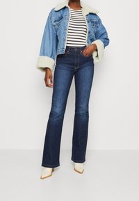 Jeansjacka med krämfärgad konstpäls vid kragen och ärmarna; mörkblå randig t-shirt; mörkblå utsvängda jeans; krämfärgade spetsiga ankelboots.