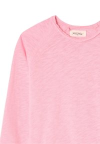 Chemise rose pâle à manches longues avec une texture douce, dotée d'un col rond et de manches raglan. Étiquette visible au niveau du col.