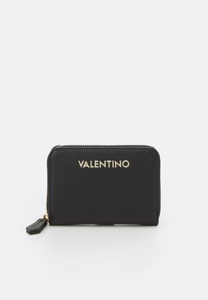 Portafoglio in pelle nera con superficie testurizzata, logo dorato "Valentino" e chiusura con zip. Presenta un pon pon nero staccabile.