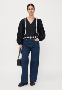 Black blouse with puff sleeves, V-neck, and white lace trim, paired with wide-leg blue jeans and black chunky boots. Small black handbag included.