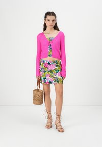 Cardigan cropped fucsia, vestito a fiori, sandali beige con lacci e borsa intrecciata. Texture morbide e colori vibranti e audaci.