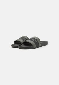 Sandale slide de culoare verde închis cu o talpă texturată neagră. Dispun de curele late cu cuvântul "DESIGNER" în negru. Design simplu, cu vârf deschis.