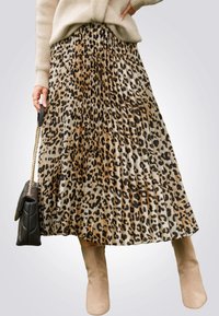 Jupe plissée en imprimé léopard dans des tons beiges et bruns, avec un design fluide. Assortie à un sac à main noir et des bottines nude.