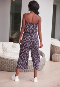 Námořnický modrý květinový overal bez ramínek, s elastickým pasem, zkrácenými nohavicemi a měkkou tkaninou. Nosený s bílými teniskami.