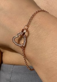 Bracciale in oro rosa con ciondolo a forma di cuore decorato con strass trasparenti, attaccato a una delicata catena con anelli.